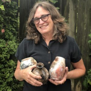 Judi Harwood holding small sagger pots, smiling