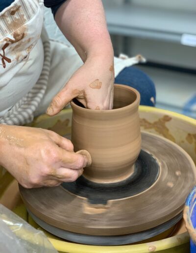 Close up student hands throwing on potters wheel, red clay