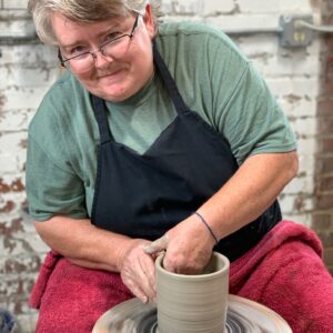 Julia Mann throwing cylinder at potters wheel, smiling
