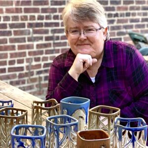 Julia Mann sitting, smiling with finished pots, pierced lanterns
