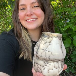 Kyra Pruitt holding her finished raku horsehair pot, smiling