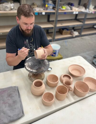 Teaching Center student waxing pots preparing for glazing, male student, beginning wheel class
